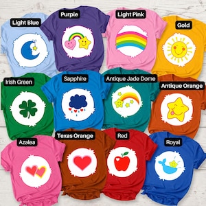 May include: A collection of twelve short-sleeved t-shirts in various colors, each featuring a circular white emblem with a unique graphic icon, including a moon, rainbow, sun, clover, cloud, heart, apple, and star, with color labels.