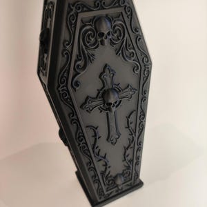 Decorative vase in the shape of a black gothic coffin with a skull and cross, perfect for Halloween.