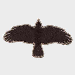 May include: A dark brown embroidered patch in the shape of a bird with its wings spread wide in flight. The bird features detailed stitching throughout its body and wings, and the entire silhouette is outlined with a light tan thread border.
