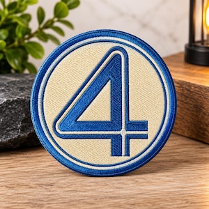 May include: A circular embroidered patch featuring a large blue number four centered on a cream-colored background. The patch is framed by a thick blue border with a thin white inner ring, showcasing detailed stitching throughout the design.