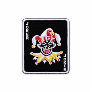 May include: A rectangular embroidered patch featuring a black background with a white border. In the center is a jester face with red and white hat details and a yellow collar. The word JOKER is embroidered vertically in white on both sides.