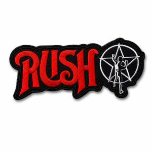 May include: An embroidered patch featuring the word RUSH in bold red lettering with a black border. To the right of the text is a white circular emblem containing a five-pointed star and a silhouette of a person with arms raised.