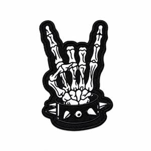 May include: A black and white embroidered patch featuring a skeletal hand making a rock and roll gesture. The hand emerges from a black studded collar with white spikes, all outlined in a thick black border against a plain white background.