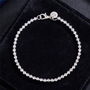 May include: A silver-toned beaded bracelet featuring small, reflective spherical beads arranged in a continuous circular chain. The bracelet includes a lobster claw clasp and a small round tag stamped with the number 925 for identification.