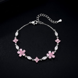 Puede incluir: Una pulsera de cadena en tono plateado con piedras preciosas rosas en forma de flor que se alternan con piedras transparentes de corte marquesa. La pulsera incluye un cierre de mosquetón y una cadena extensora con un pequeño dije metálico plano.