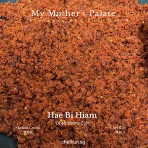 May include: A textured mixture of deep red Hae Bi Hiam dried shrimp chilli paste. The text My Mother's Palate Flavours She Left Me, Hae Bi Hiam Dried Shrimp Chilli, Madam Cecilia, Chef Kün, and chefkun.sg are printed in white over the food.