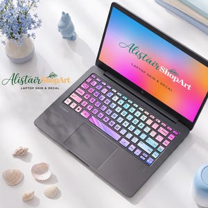 May include: A dark gray laptop featuring a keyboard skin with a pink and blue gradient color scheme. The screen displays a vibrant pink, purple, and blue gradient background with the text Alistair ShopArt LAPTOP SKIN & DECAL in white lettering.