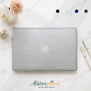 Puede incluir: Una pegatina de metal cepillado plateado para portátil aplicada sobre un ordenador Dell, con una textura horizontal. El diseño incluye un recorte circular para el logotipo de Dell en el centro. Cuatro muestras de color circulares aparecen arriba.