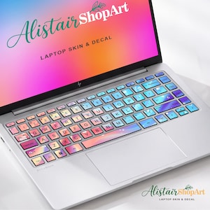 May include: A silver laptop featuring a keyboard skin with a gradient of blue, purple, and pink hues. The screen displays a vibrant pink and orange background with the text AlistairShopArt LAPTOP SKIN & DECAL in green and white lettering.