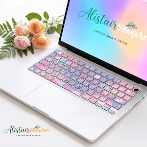 May include: A silver laptop featuring a keyboard cover with a pastel pink, blue, and purple cloud pattern and alphabet letters. The screen displays the text AlistairShopArt LAPTOP SKIN & DECAL against a soft, multi-colored gradient background.