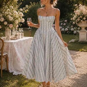 May include: A midi-length dress featuring a white base with vertical light green stripes and small pink floral patterns. The dress has a fitted bodice with a square neckline, thin spaghetti straps, and a full, pleated skirt. The text Boh&eacute;sia is visible.