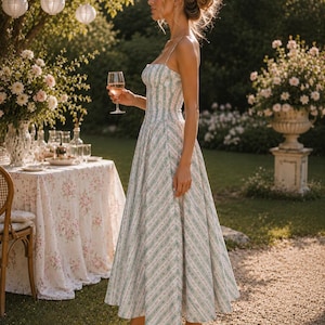 May include: A midi-length dress featuring a white base with vertical stripes in light green and small pink floral patterns. The garment has a fitted bodice with a square neckline, thin spaghetti straps, and a flared skirt. The word Boh&eacute;sia is visible.