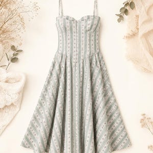 May include: A midi-length dress featuring a sweetheart neckline and thin spaghetti straps. The fabric is light green with vertical white stripes and a delicate floral pattern. The bodice is fitted, transitioning into a flared, pleated skirt.