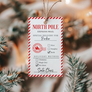 Puede incluir: Una etiqueta de regalo rectangular con un borde de rayas diagonales rojas y blancas. El texto dice North Pole Express Mail, Special Delivery for Parker y Santa Claus. Incluye un sello rojo, casillas para Nice, Naughty, Both y métodos de entrega como Chimney, Magic key o Pet door.