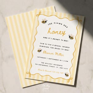 Puede incluir: Una tarjeta de invitación rectangular para despedida de soltera con reverso de rayas amarillas y blancas y frente blanco con borde dorado festoneado, ilustraciones de abejas y el texto She found her honey and it's meant to bee.