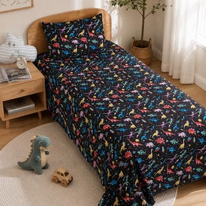 May include: A single bed set featuring a black background with a colourful pattern of various dinosaurs, planets, and stars. The set includes a fitted sheet, a flat sheet, and a matching pillowcase, all displaying the same vibrant space-themed dinosaur print.