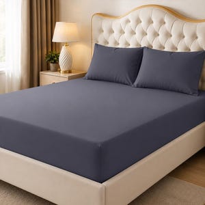 May include: A solid dark gray fitted sheet covering a mattress, paired with two matching dark gray rectangular pillowcases. The bedding set features a smooth, matte fabric texture and is displayed on a tufted, cream-colored upholstered bed frame.