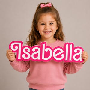 May include: A custom-cut sign featuring the name Isabella in a bold, stylized pink font with a thick white outline. The lettering is connected in a single piece, designed for display as a decorative name plaque or personalized signage.