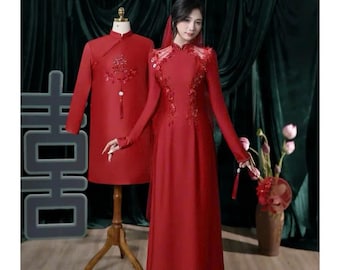 May include: A red long-sleeved gown with intricate floral embroidery and a matching red tunic on a mannequin. The gown features a high neckline and a sheer red veil. The tunic displays a central embroidered design and a hanging tassel detail.