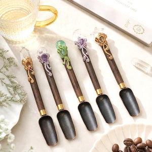 Può includere: Cinque cucchiai con manici in legno scuro e coppe in metallo nero opaco. Ogni manico presenta un design metallico a forma di vite che avvolge una pietra preziosa unica, tra cui pietre trasparenti, viola, verdi e color ambra.