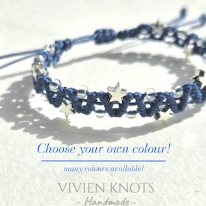 May include: A navy blue macrame bracelet featuring silver-toned star charms and clear beads woven into the cord. The text on the image reads: Choose your own colour! many colours available! VIVIEN KNOTS - Handmade -