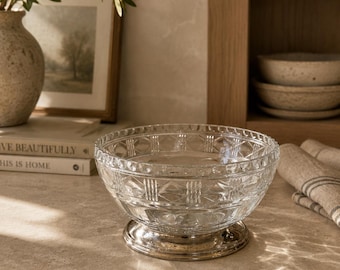 May include: A clear glass bowl featuring a detailed diamond-cut geometric pattern on its exterior surface. The bowl is supported by a circular, polished metallic base that provides a stable foundation for the transparent, textured glass vessel.