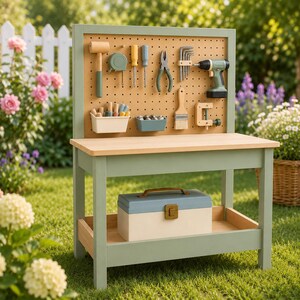 May include: A sage green wooden toy workbench featuring a pegboard back panel with various toy tools including a hammer, pliers, drill, and screwdrivers. A storage shelf below holds a two-toned blue and cream toy toolbox with a metal latch.