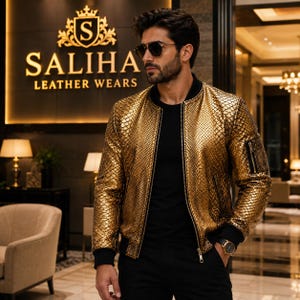 May include: A metallic gold bomber jacket with a textured snakeskin pattern, featuring a black ribbed collar, cuffs, and hem. The jacket has a front zip fastening and a small zipped utility pocket on the left sleeve, worn over a plain black shirt.