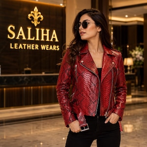 Könnte beinhalten: Eine rote und schwarze Leder-Motorradjacke mit Schlangenledermuster, Reverskragen, silberfarbenen Metallreißverschlüssen und einem Gürtel mit Schnalle am Saum. Die Jacke wird über einem schwarzen Oberteil und einer schwarzen Hose getragen.