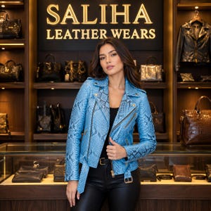 Puede incluir: Una chaqueta de motorista azul claro con estampado de piel de serpiente negra, con cremalleras doradas, solapa con muescas y cintura con cinturón. La chaqueta se lleva sobre un top y pantalones negros, con el texto SALIHA LEATHER WEARS visible detrás.