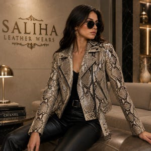 Könnte beinhalten: Eine Lederjacke mit Schlangenledermuster, fallendem Revers, langen Ärmeln und Frontreißverschluss. Die Jacke verfügt über einen Gürtelsaum mit Metallschnalle und schwarzen Beschlägen und wird über einem schwarzen Oberteil und Lederhose getragen.