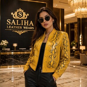 Peut inclure: Un blouson style bomber à motif peau de serpent jaune et noir avec une fermeture éclair frontale, des poignets côtelés et un ourlet côtelé. Le blouson est porté sur un haut noir et un pantalon noir, avec des lunettes de soleil teintées.