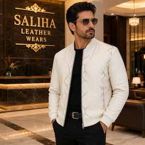 May include: A white bomber jacket with a textured snakeskin pattern, featuring a ribbed collar, cuffs, and hem, a central silver zipper, and long sleeves. The jacket is worn over a plain black t-shirt and black trousers with a black leather belt.
