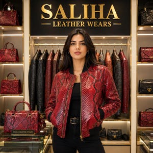 Könnte beinhalten: Eine rote und schwarze Leder-Bomberjacke mit Schlangenledermuster, Frontreißverschluss sowie schwarzem Rippstrickkragen und -bündchen. Sie wird über einem schwarzen Oberteil und einer schwarzen Hose mit Gürtel in einem Geschäft mit der Aufschrift SALIHA LEATHER WEARS getragen.