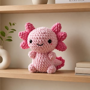 Peut inclure: Une peluche axolotl crochetée rose clair avec une finition en fil texturé doux. La créature présente de grands yeux noirs en plastique, une bouche souriante cousue, deux branchies externes plumeuses sur chaque côté de la tête et une queue.