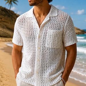 Puede incluir: Una camisa blanca de manga corta con botones, textura de ganchillo abierta, cuello clásico y un bolsillo en el pecho. La prenda está confeccionada con un patrón de rejilla y se lleva con un collar de cadena plateada sencillo.