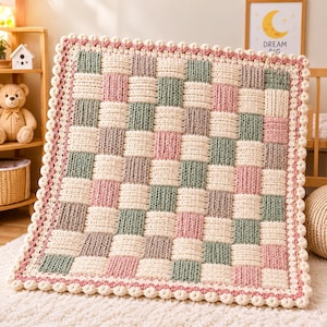 May include: A square crochet blanket featuring a basketweave pattern in alternating blocks of cream, sage green, and dusty rose. The blanket is finished with a decorative scalloped border in cream and dusty rose, creating a textured finish.