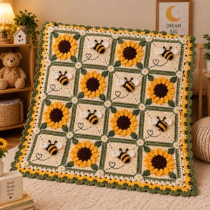 May include: A square crochet blanket featuring a grid of alternating squares with yellow sunflowers and black and yellow bumblebees on a cream background, framed by dark green borders and small white flowers, finished with a scalloped green edge.
