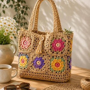 May include: A beige crochet tote bag constructed from joined square panels, each featuring a colorful floral motif in shades of pink, yellow, and purple. The bag includes two top handles and a central wooden button closure with a hanging tassel.