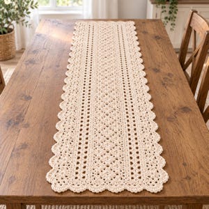 May include: A long, rectangular cream-colored crochet table runner featuring an intricate, repeating floral and geometric pattern. The runner has a scalloped edge design that runs along both sides and ends, creating a decorative border.
