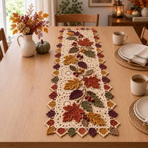 May include: A cream-colored crocheted table runner featuring an intricate lace pattern and a central decorative vine motif. The runner is adorned with three-dimensional crocheted autumn leaves in shades of orange, red, brown, and green.