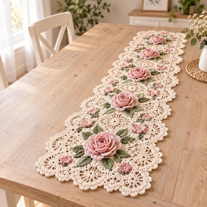 May include: A long, rectangular crochet table runner in cream yarn featuring a repeating pattern of three-dimensional pink roses and small green leaves. The runner has a scalloped edge with intricate lace-like circular motifs throughout the design.