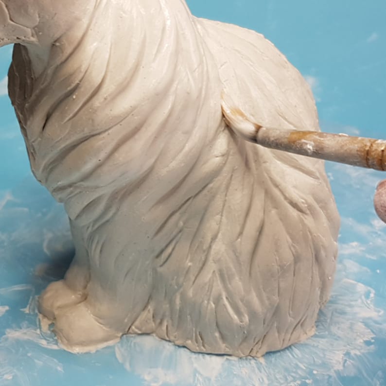 Peut inclure: Une figurine de chat en c&eacute;ramique blanche avec une texture de fourrure d&eacute;taill&eacute;e en cours de peinture avec un pinceau.