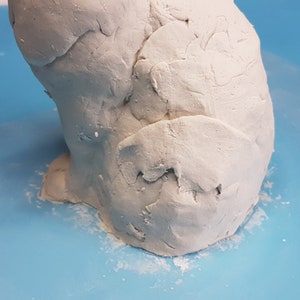 Peut inclure: Gros plan sur une sculpture en argile blanche d'un lapin, montrant les d&eacute;tails textur&eacute;s de la fourrure. La sculpture est pos&eacute;e sur une surface bleue.
