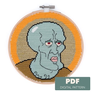 May include: A cross-stitch embroidery hoop depicting a cartoon character with a light blue face, red eyes, and a sad expression. The design is set against a yellow and tan background, with a brown border. The text "PDF DIGITAL PATTERN" is in the lower right corner.