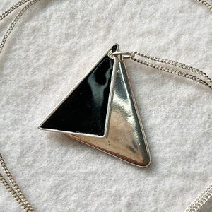 May include: A silver chain necklace with a black and silver triangle pendant.
