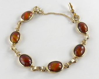 May include: A gold bracelet with a chain and six oval-shaped brown and orange stones.