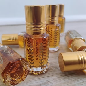 May include: A collection of small, hexagonal glass perfume bottles with gold-colored screw-on caps. Each clear glass bottle contains an amber-colored liquid and features a delicate, etched botanical pattern of leaves and berries on its exterior.