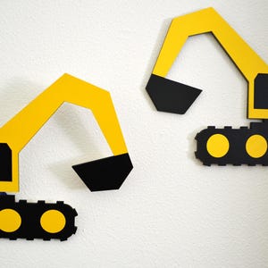 May include: Two flat, wall-mounted excavator cutouts made of yellow and black material. Each construction vehicle features a long articulated arm with a black bucket, a yellow cab with black window details, and a black track base with yellow wheels.