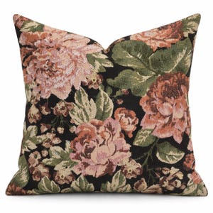 May include: A square throw cushion featuring a woven tapestry design with a black background. The pattern displays large, detailed floral motifs in shades of dusty pink, muted orange, and various tones of sage and olive green leaves.